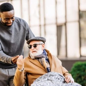An adult male pushing an older male in a wheelchair, caregiver